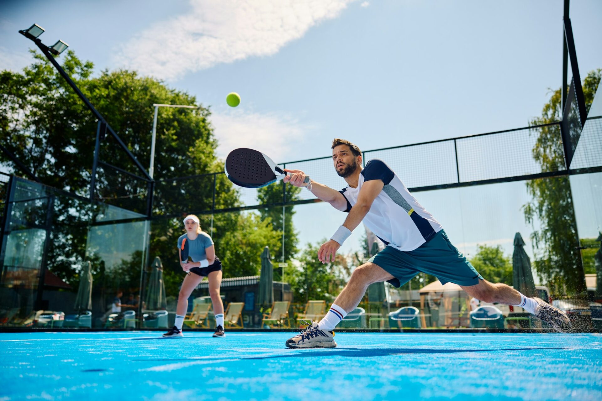 Paddle tennis player making an effort to while hitting the ball during a match on outdoor court.